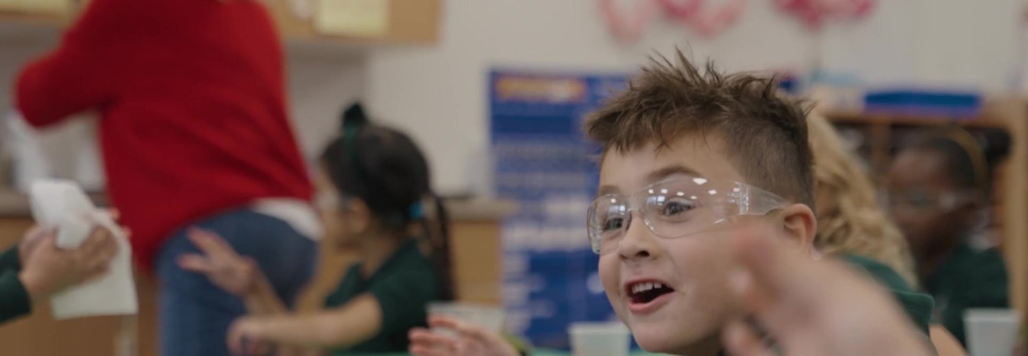 Young student in safety goggles smiling during a hands-on science lesson in a school classroom